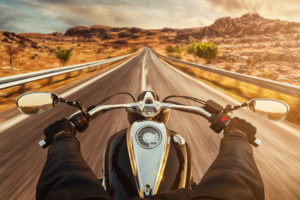 driver riding a motorcycle on an empty road in the desert