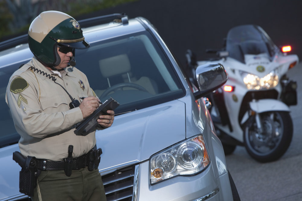 policeman writing a ticket in front of an suv with his motorcycle in background