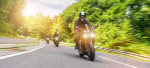 motorcycle riders coming around a curve on a forest roadway