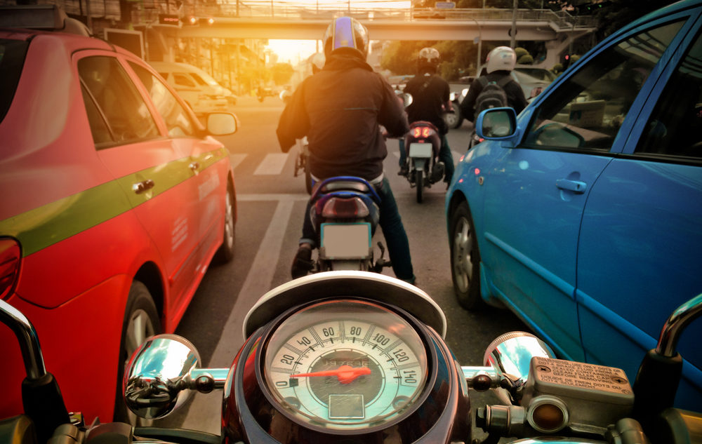 motorcycles with speedometer riding between cars on the street