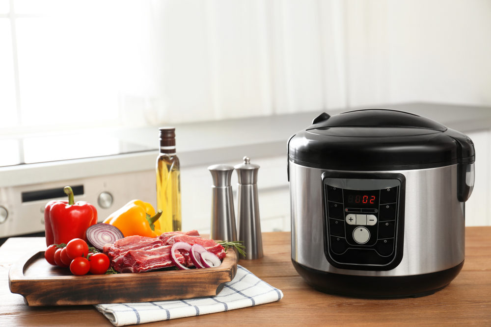 Modern multi cooker and products on wooden table in kitchen