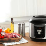 Modern multi cooker and products on wooden table in kitchen