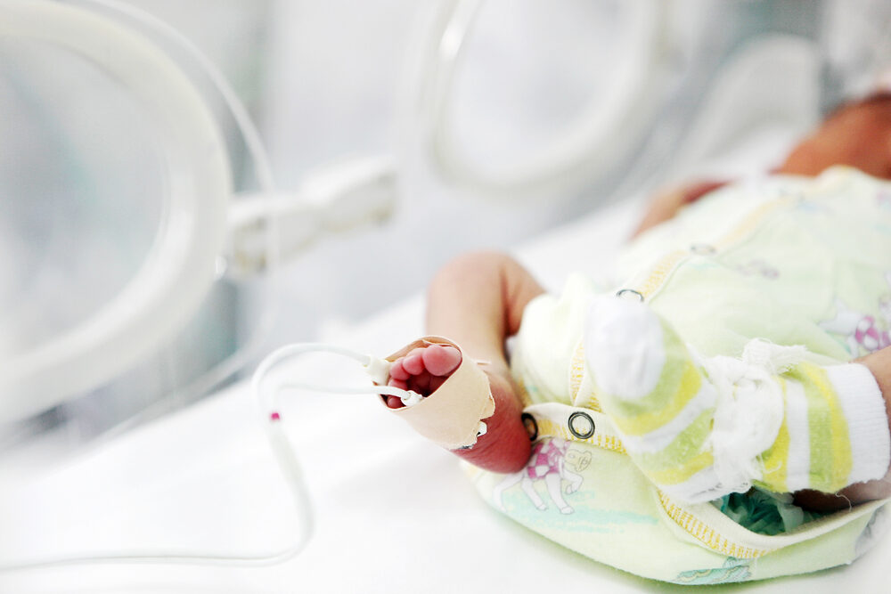 a newborn in an incubator after suffering birth injuries connected to monitors with foot bandaged