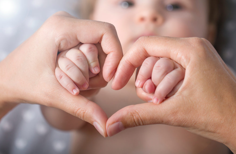 Newborn baby holding mother hands in heart shape 