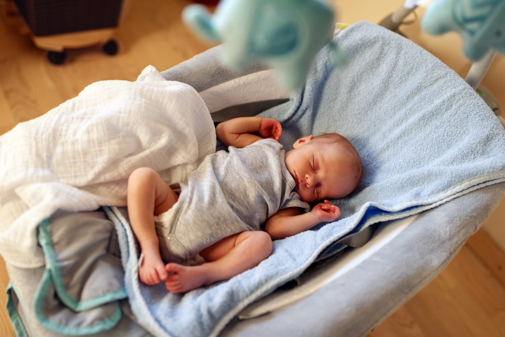 Adorable newborn boy sleeping in bouncer chair and dreaming