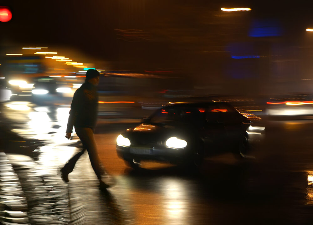 a pedestrian crossing the street at night with oncoming cars
