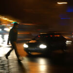 a pedestrian crossing the street at night with oncoming cars