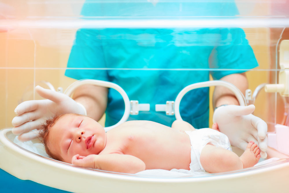 Medical staff taking care of newborn baby in infant incubator