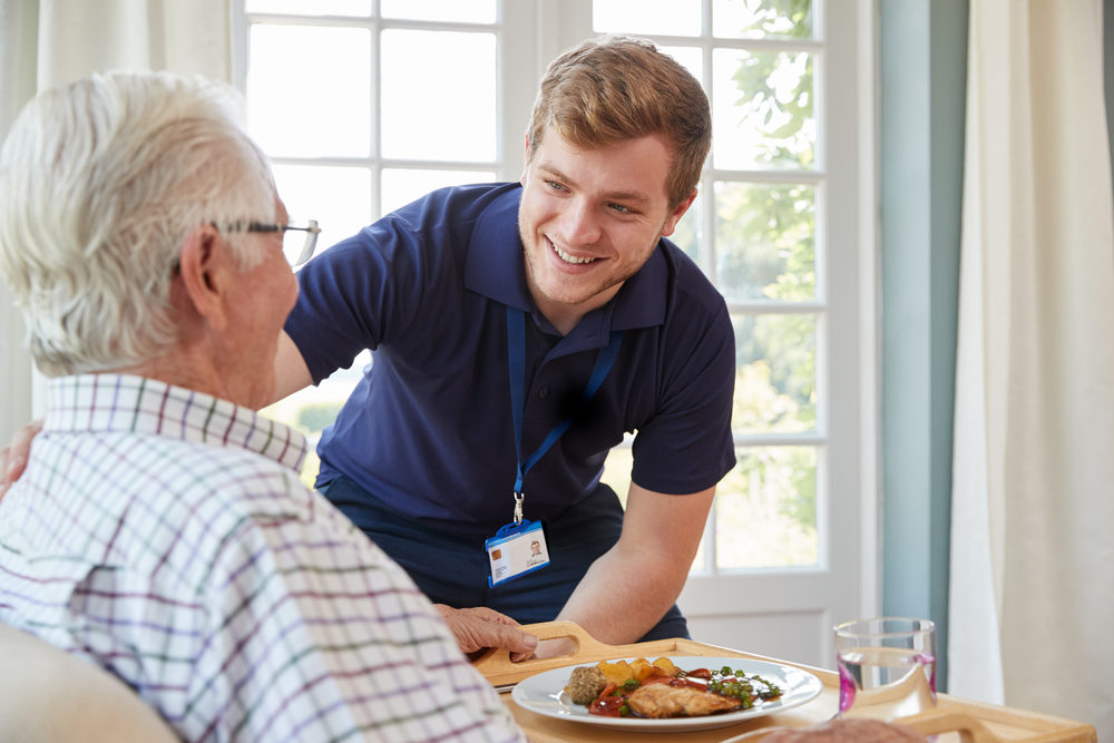 Milestone Takes Action in the Community An elderly man is served dinner by a young male nurse at a home