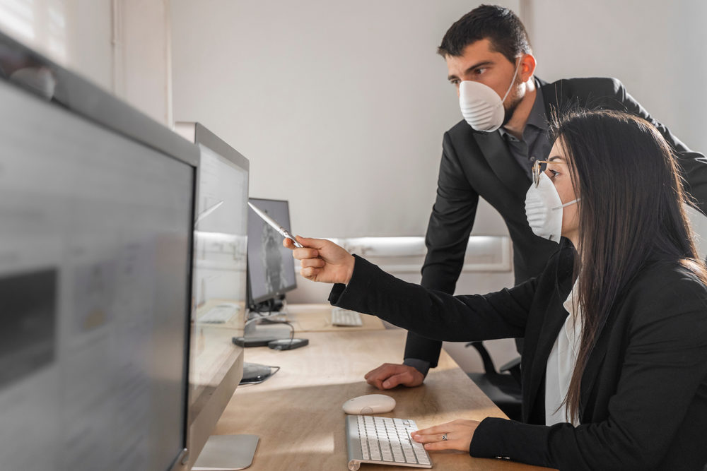 Man and woman in office during coronavirus wearing masks at computers