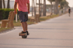 Man rides on electric onewheel skateboard on sidewalk at beach