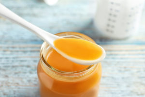 Jar and spoon with orange baby food on wooden table