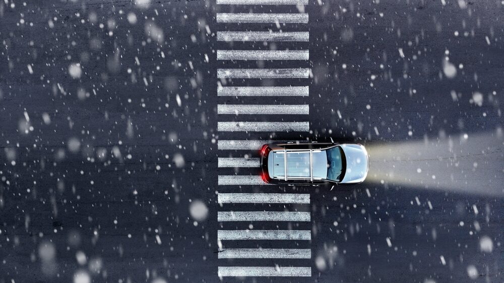 aerial view of an suv driving through a pedestrian crossing while it snows