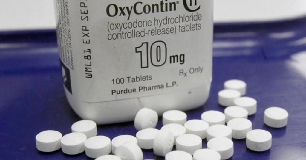Small white pills surround a bottle of OxyContin