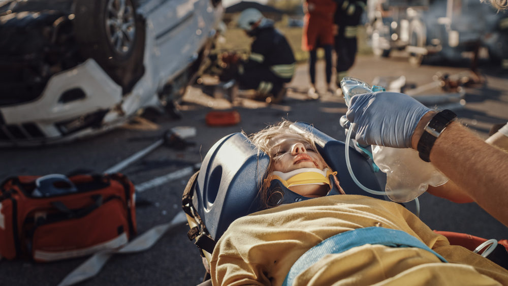 paramedics applying an oxygen mask to a child in a stretcher at an accident scene