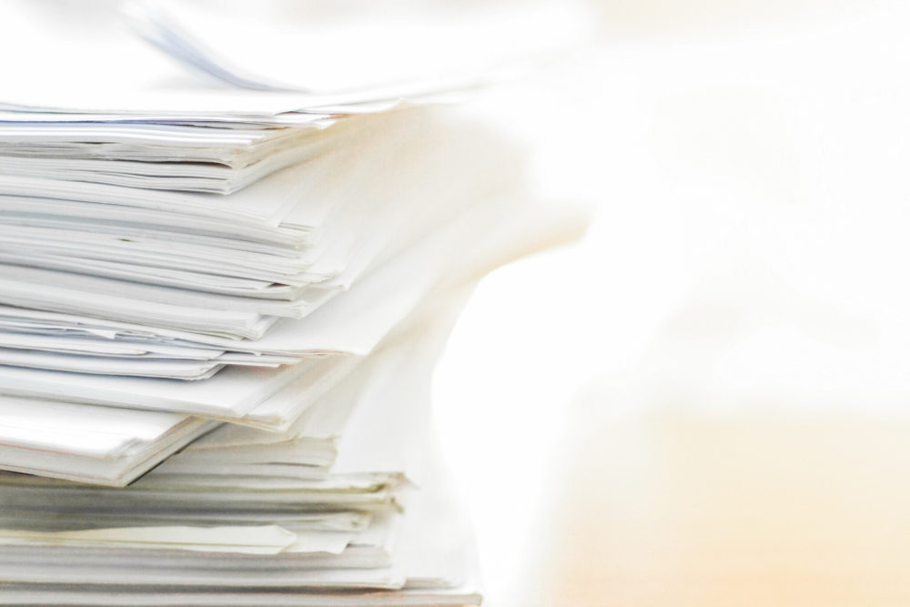 Large stack of white papers piled on a desk