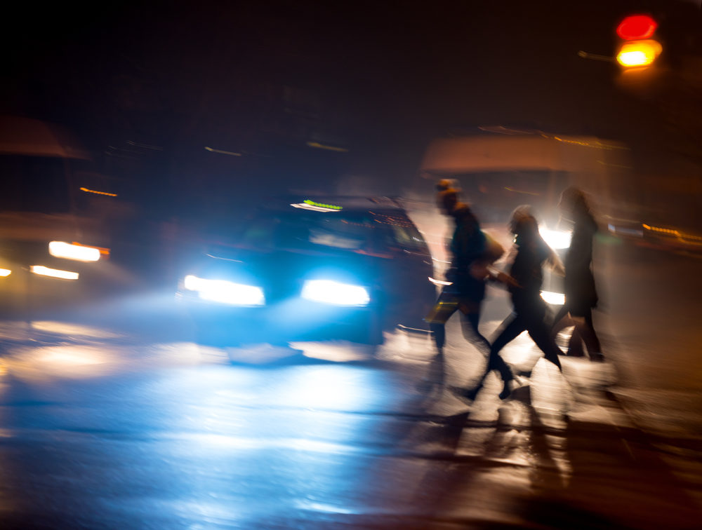 group of pedestrians crossing the street at night with cars waiting to continue