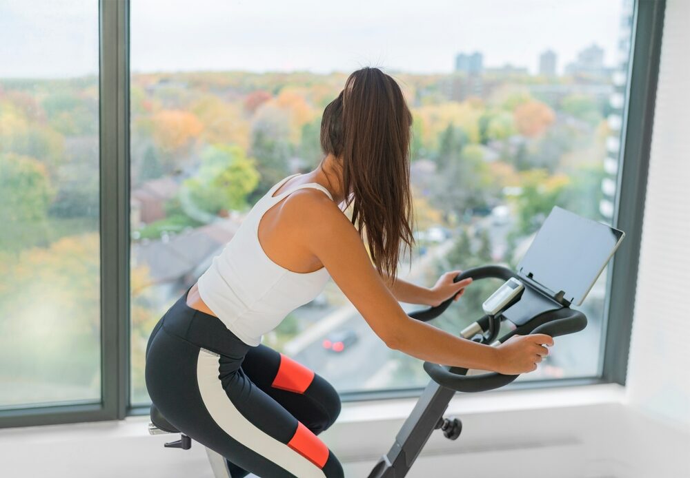woman exercising at home indoor cycling with online class on screen.