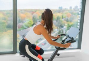 woman exercising at home indoor cycling with online class on screen.