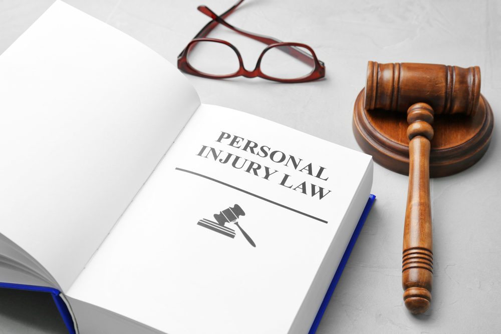 Book with words PERSONAL INJURY LAW, gavel and glasses on grey background