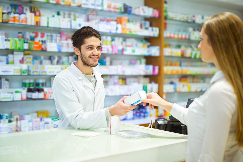 A male pharmacist hands a customer medications over the counter