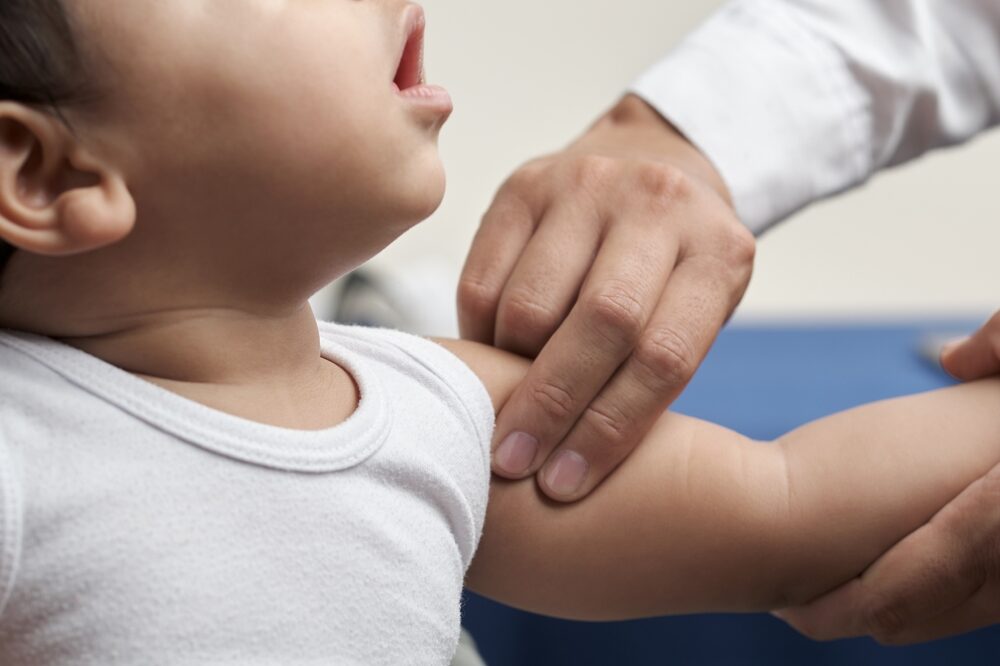 physician's hands palpating humeral brachial pulse in infant patient