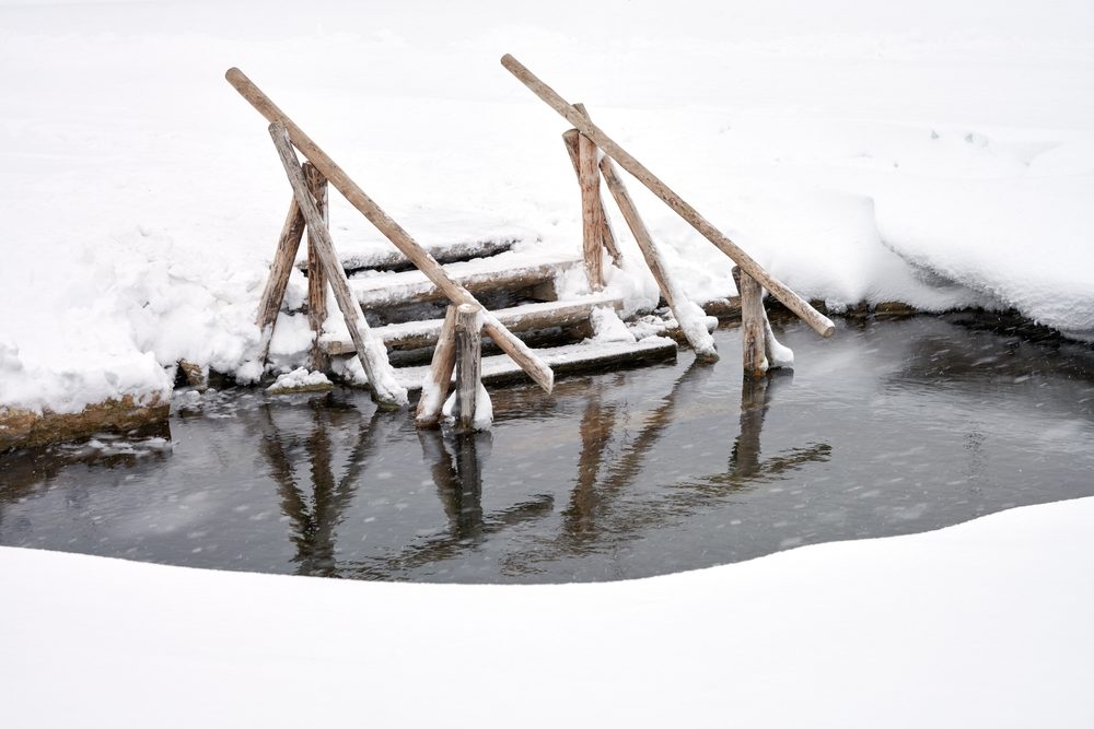 An ice hole on a frozen pond with a snow-covered ladder descending into the water.