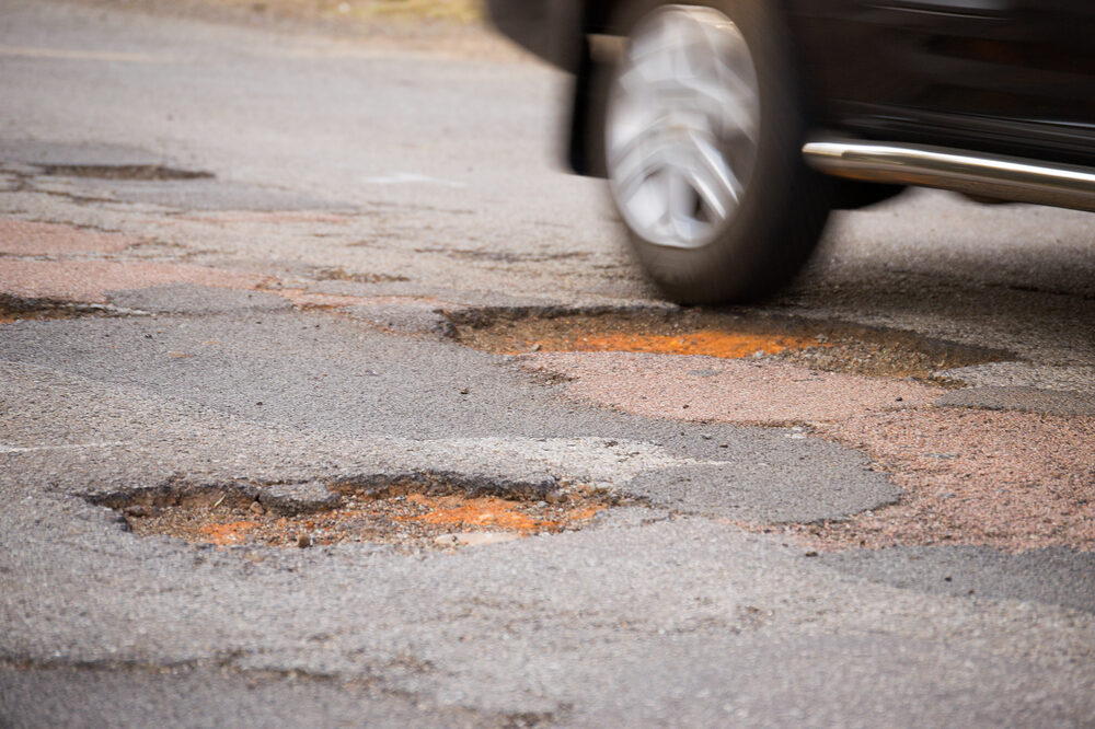 Rear wheel of a moving car about to drive into a pothole on roadway