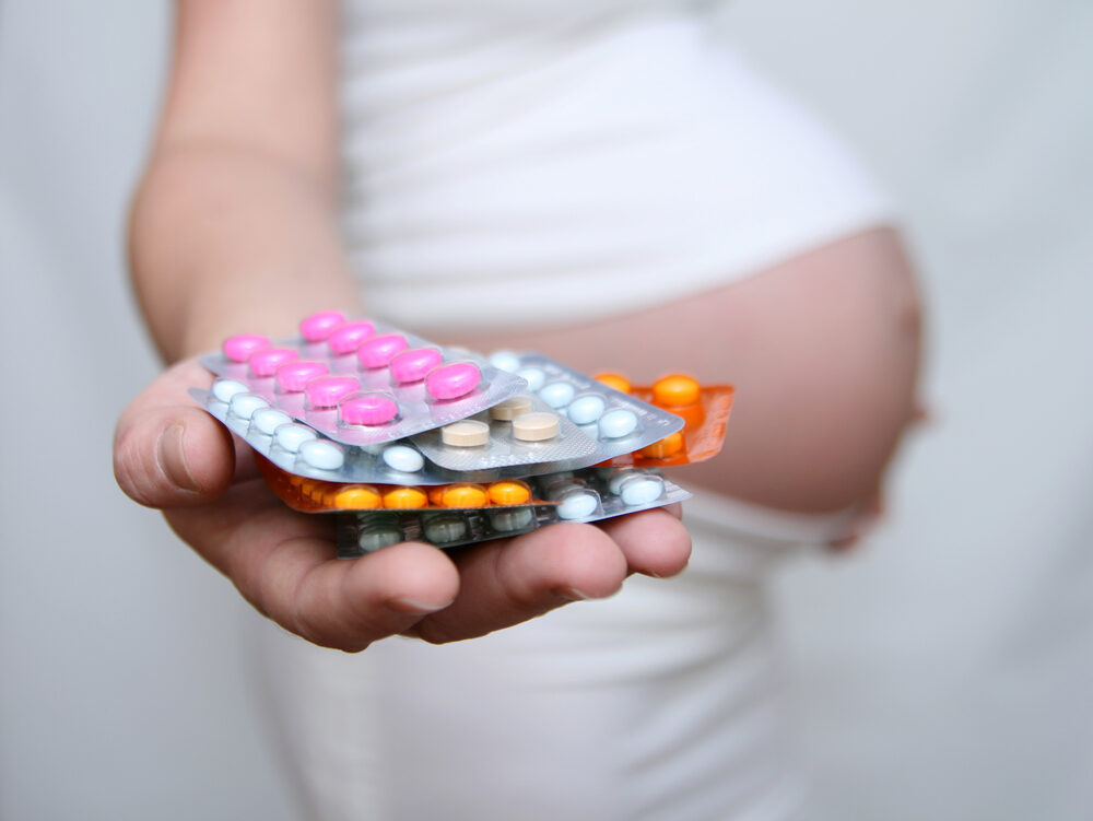 hand of a pregnant woman holding various medicine