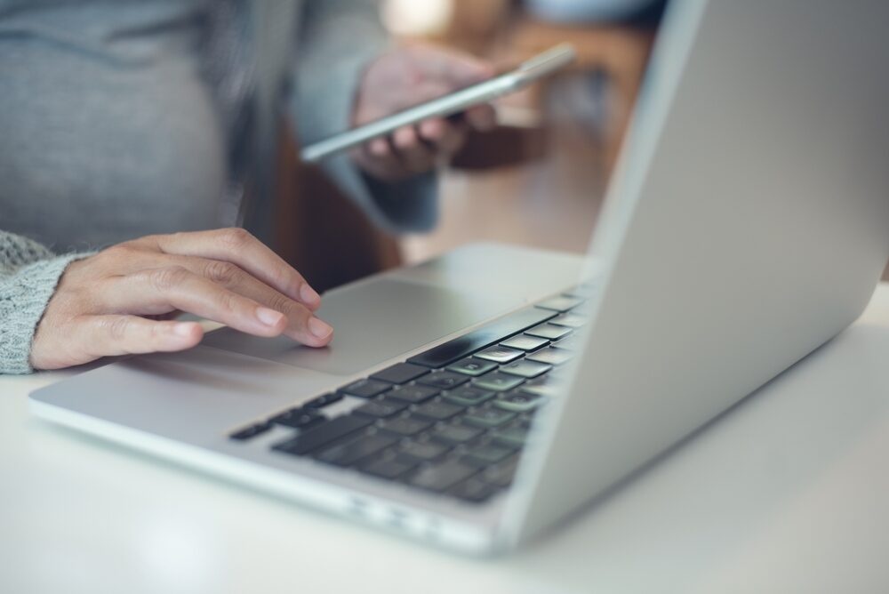 Dangerous Recalled Products Still For Sale on Social Media Platforms a pregnant woman sitting at a desk with a laptop and her smartphone shopping on social media