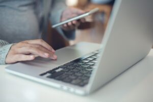 a pregnant woman sitting at a desk with a laptop and her smartphone shopping on social media