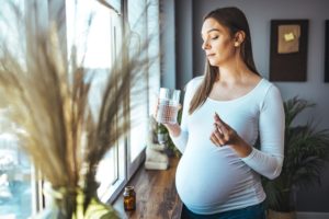 A young pregnant woman is taking medications and drinking water.