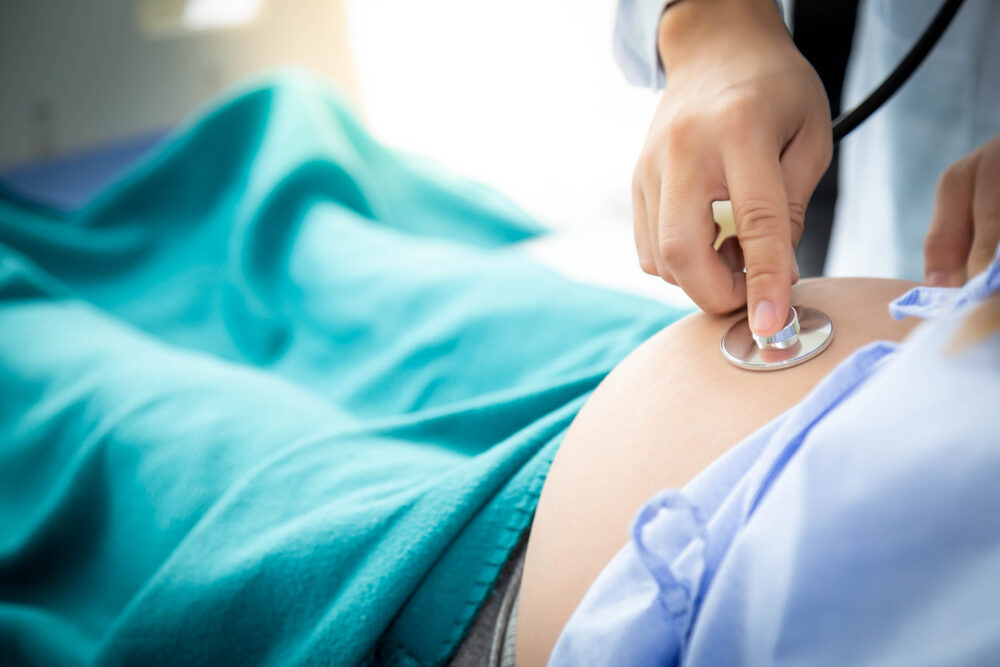 Doctor or Obstetrician listen fetus heartbeat and examine fetus position on Pregnant mother belly by using stethoscope at hospital.