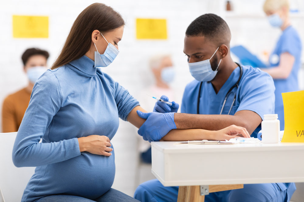 Research Shows COVID-19 Vaccine Safe for Pregnant Women African American Doctor Giving Coronavirus Vaccine Injection Shot To Pregnant Woman, Wearing Protective Face Mask In Clinic Hospital.