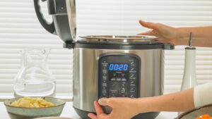 closeup of a woman pressing button on a pressure cooker with the lid open on kitchen counter