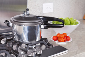 double valve pressure cooker on stove near vegetables