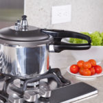 double valve pressure cooker on stove near vegetables