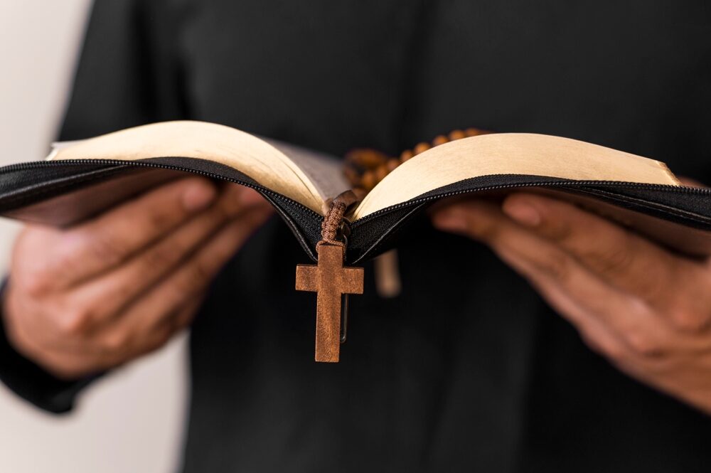 closeup of priest holding a bible with rosary beads hanging over the side