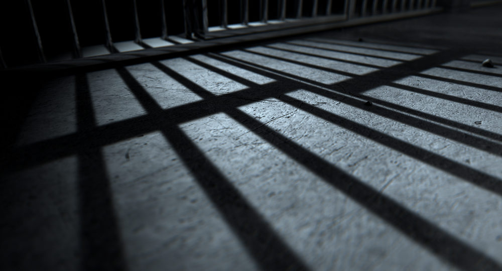 A closeup of view of a jail cells iron bars casting shadows on the prison floor