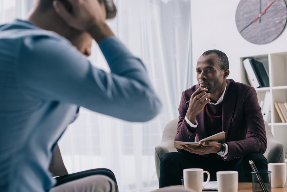 A counselor listens intently to a male patient in his office