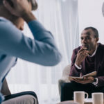 A counselor listens intently to a male patient in his office