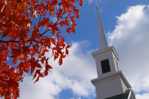 leaves that have turned red and church steeple against a blue sky