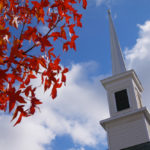 leaves that have turned red and church steeple against a blue sky