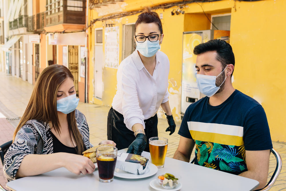 Clients with masks on the terrace of a bar in Spain attended by a waiter with gloves and masks.