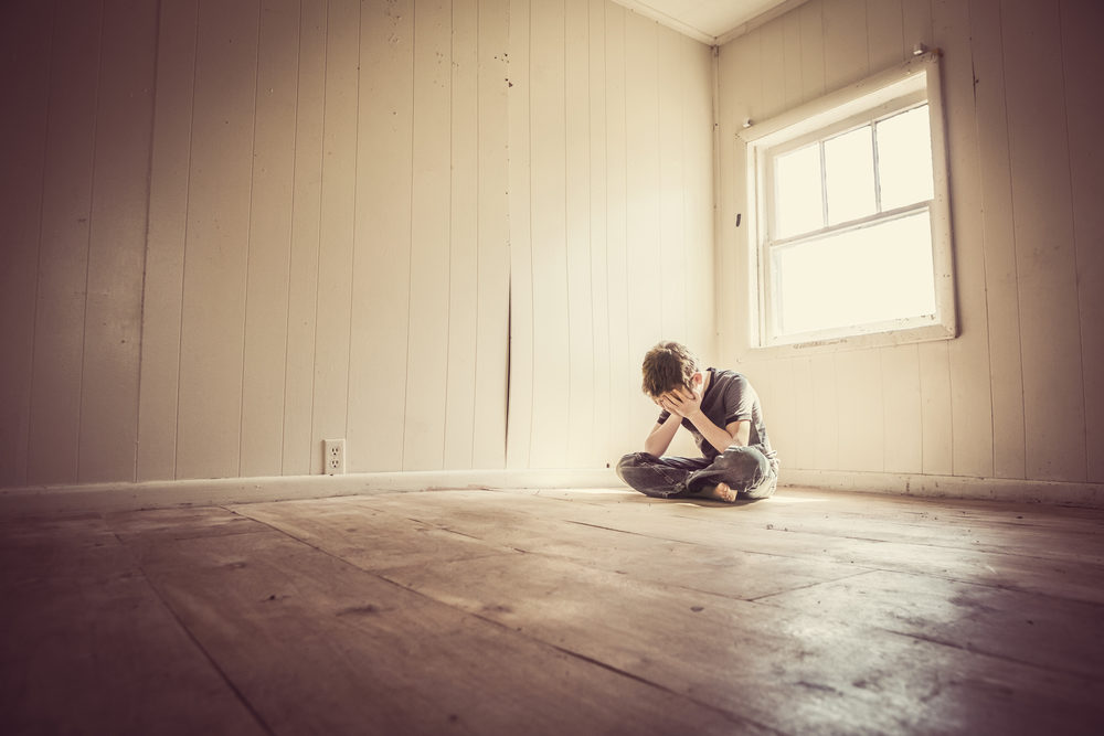 a boy with his hands over his face alone in a room