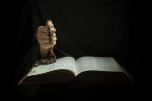 closeup of Hands holding rosary beads and cross while reading bible