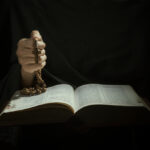 closeup of Hands holding rosary beads and cross while reading bible