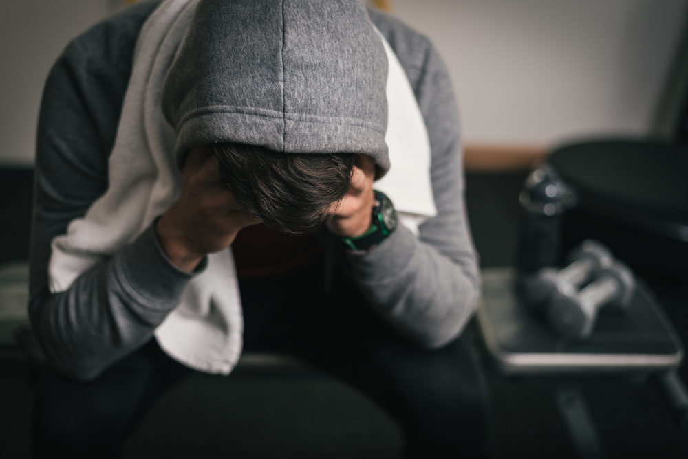 Strong sporty man sitting on gym bench suffering breakdown to overcome.