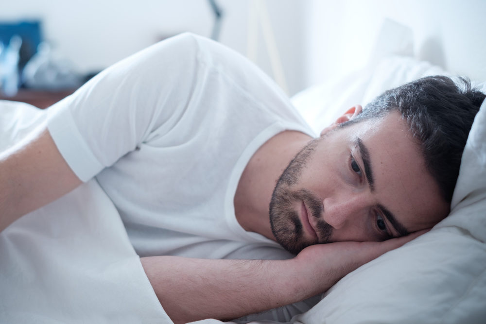 A depressed looking man lies in bed deep in thought