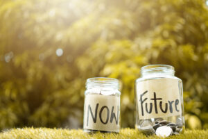 glass jars labeled now and future with coins in them representing savings on grass outside
